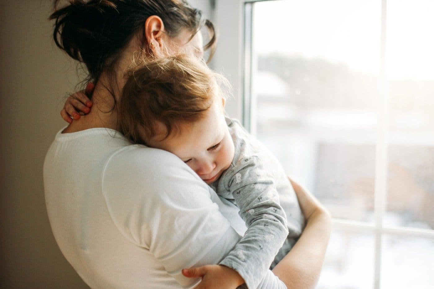 A mum holds her toddler son as she stares out a window