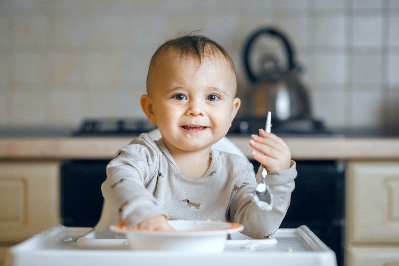 A baby eats yogurt for breakfast