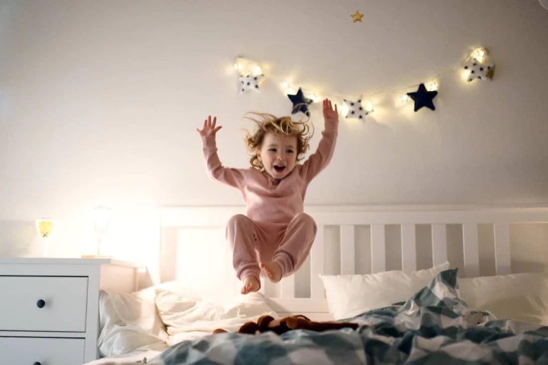 A toddler girl jumps on a bed